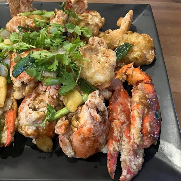 Close-up of fried lobster with green onions, cilantro, and garlic on a black plate.