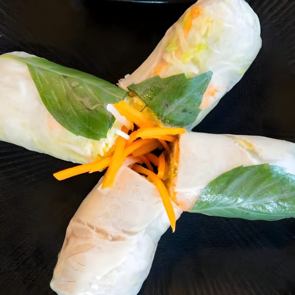 Two fresh Vietnamese spring rolls, filled with carrots and greens, crossed on a dark plate.