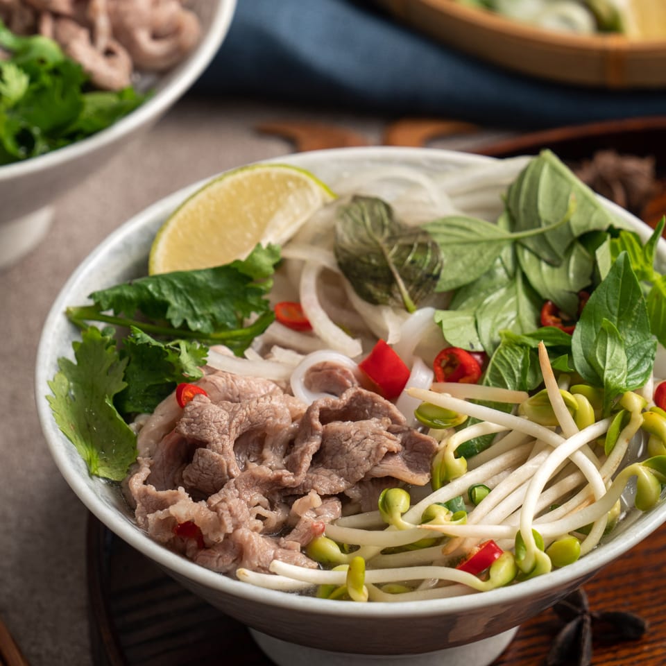Close-up of Pho City's Vietnamese pho with beef, noodles, bean sprouts, herbs, and lime.